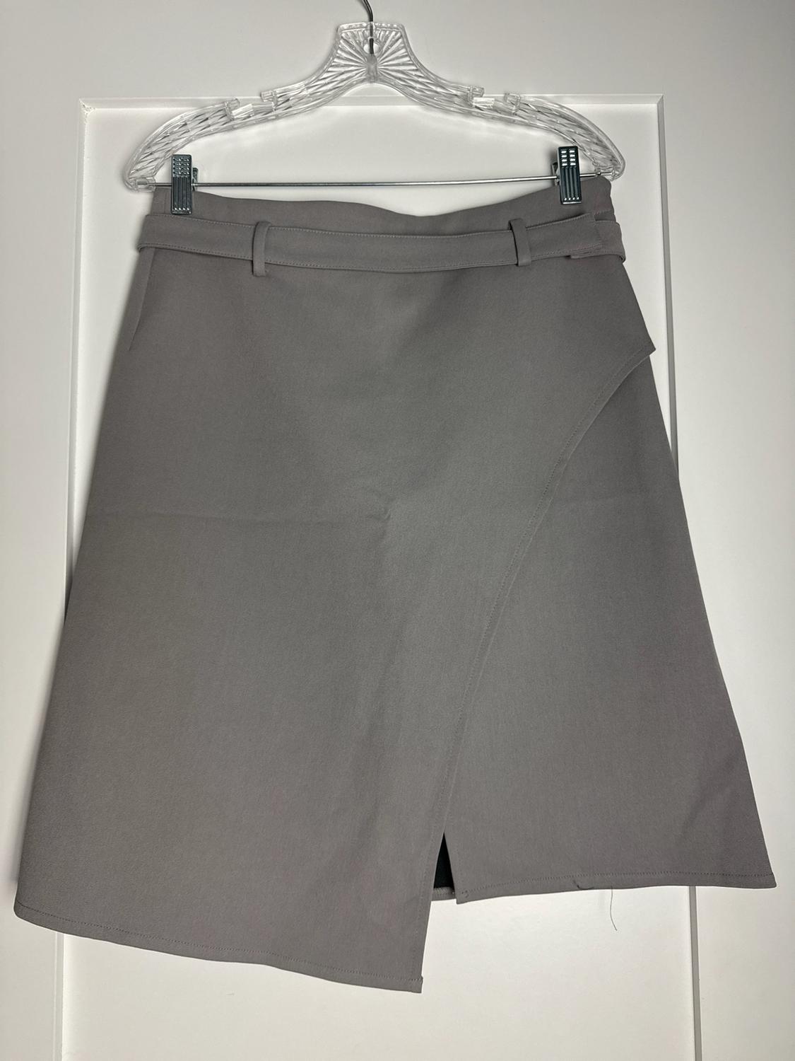 Grey asymmetric wrap-over skirt with a front split and belt loops, hanging on a clear hanger over a white door.