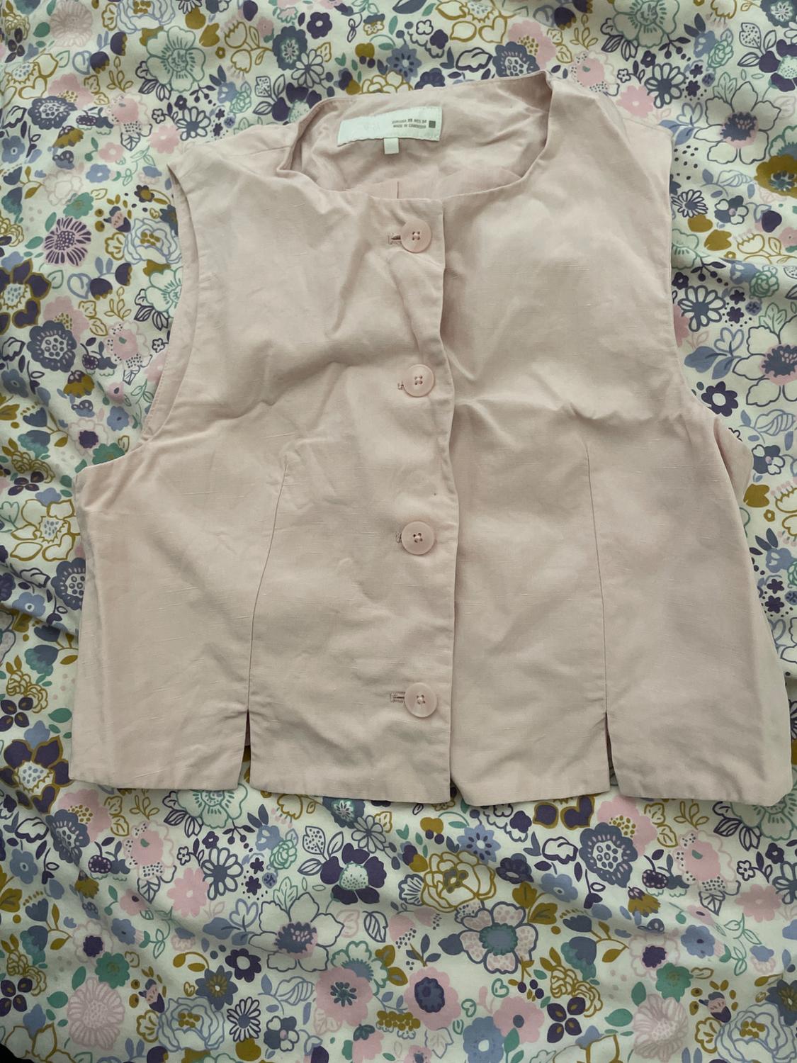 Light pink sleeveless waistcoat with buttons, over a floral print fabric in pastel and blue tones.