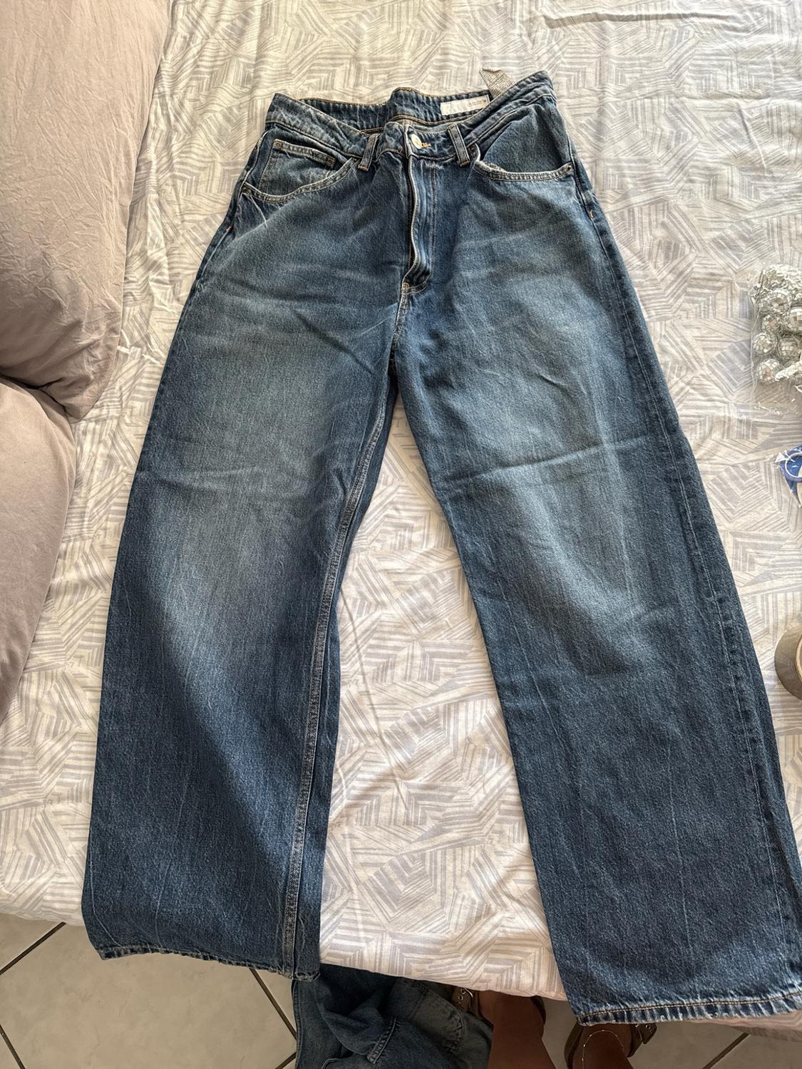 Blue wide-leg jeans laid out on a bed with geometrically patterned sheets. Casual and relaxed atmosphere.