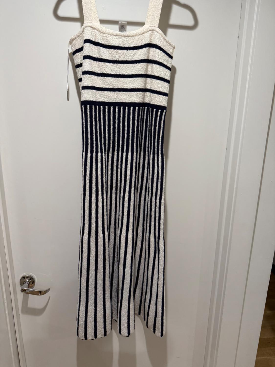 White knit dress hanging on a door. It has horizontal dark stripes on the top and vertical ones on the skirt.