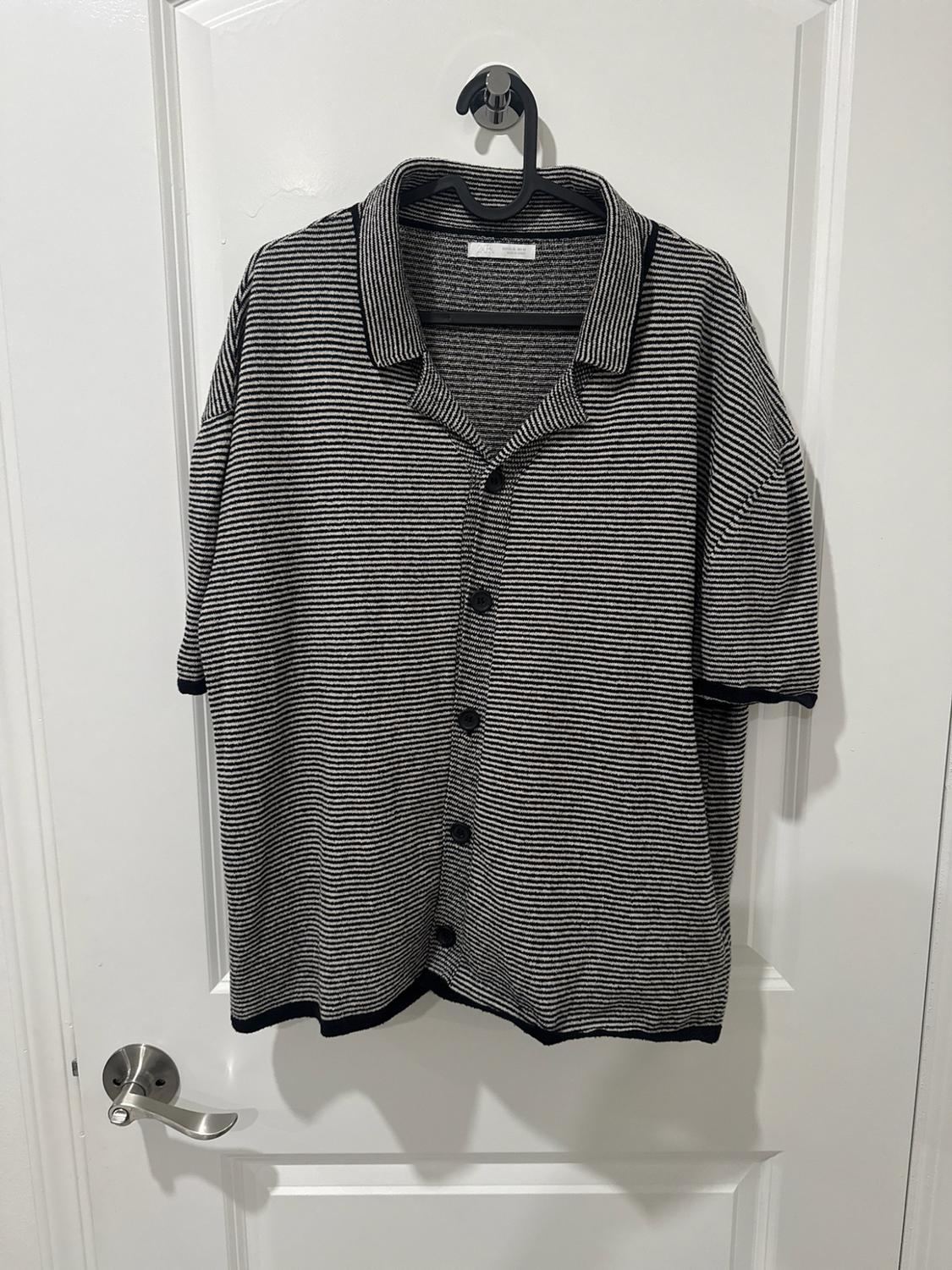 Short-sleeve shirt with horizontal black-and-white stripes and a button closure, hanging on a hanger over a white door.