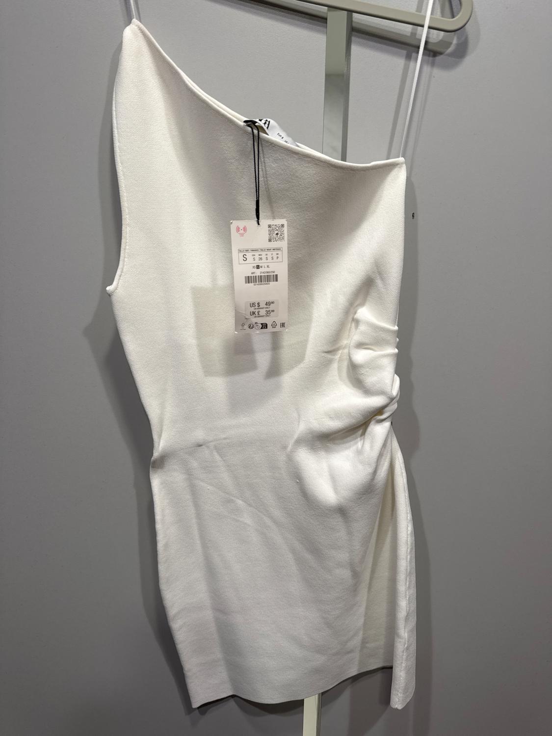 Asymmetrical white dress hanging on a gray hanger, with visible price tag indicating US$ 49.99, UK£ 35.99.