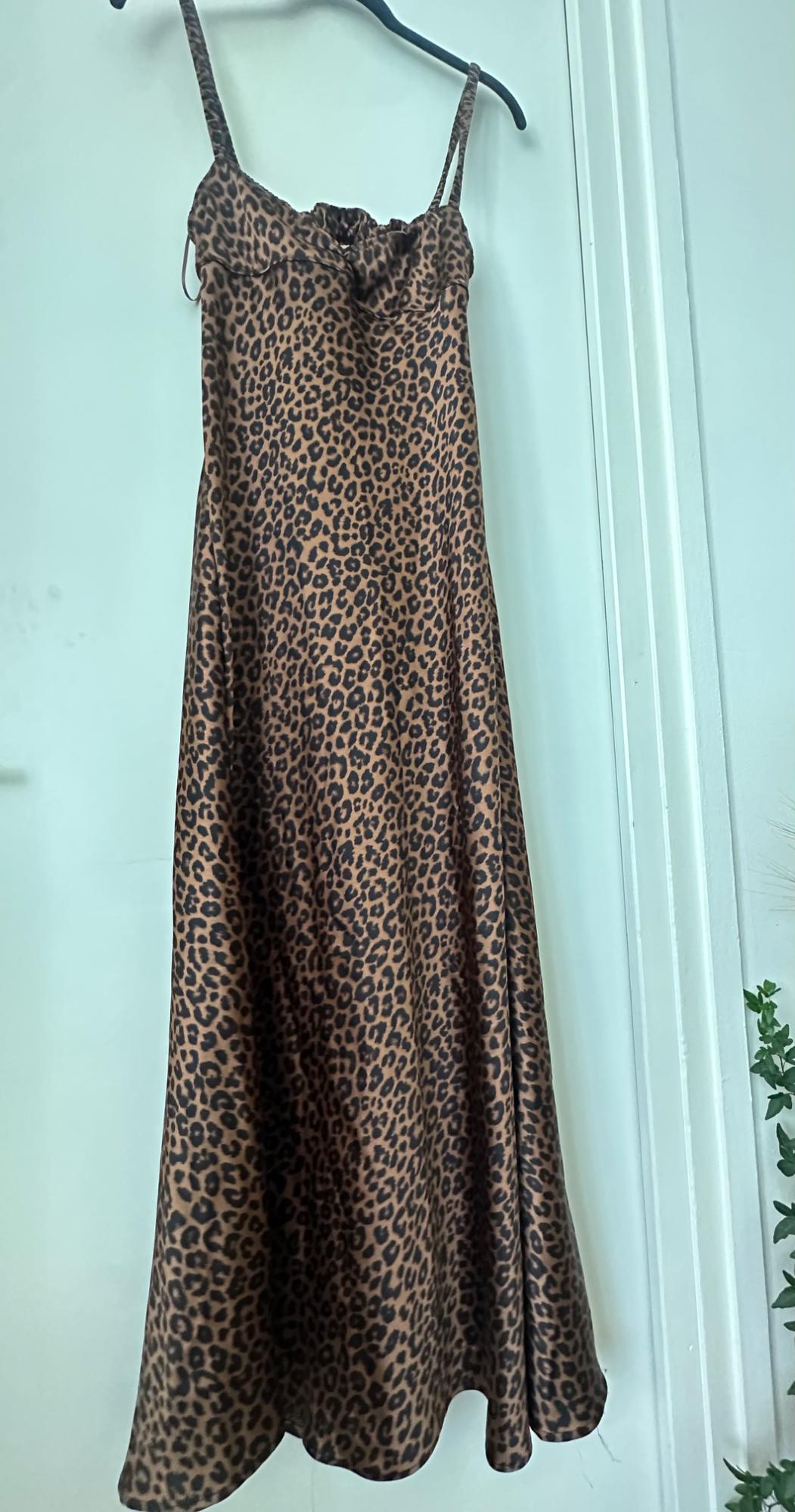 Long leopard print camisole dress hanging on a black hanger on a white door. Green leaves peek in from the right.