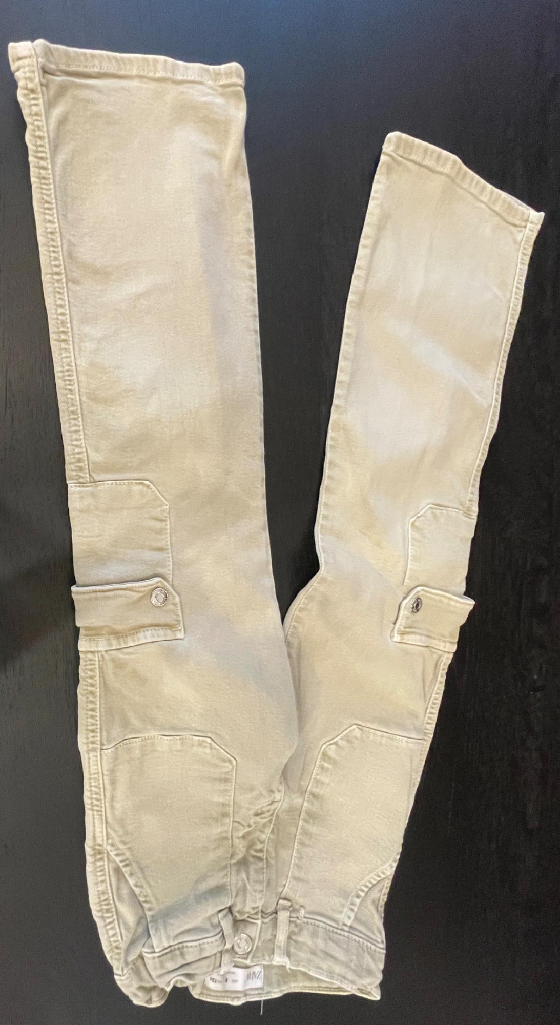 Beige cargo trousers with side pockets, laid out in a relaxed style on a dark surface. Label with the text ZARA.