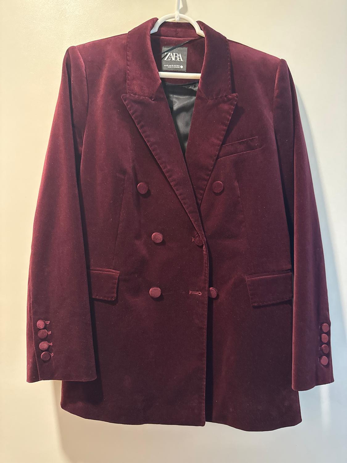 Double-breasted burgundy velvet jacket with wide lapels, hanging on a white hanger. Visible tag: Zara.