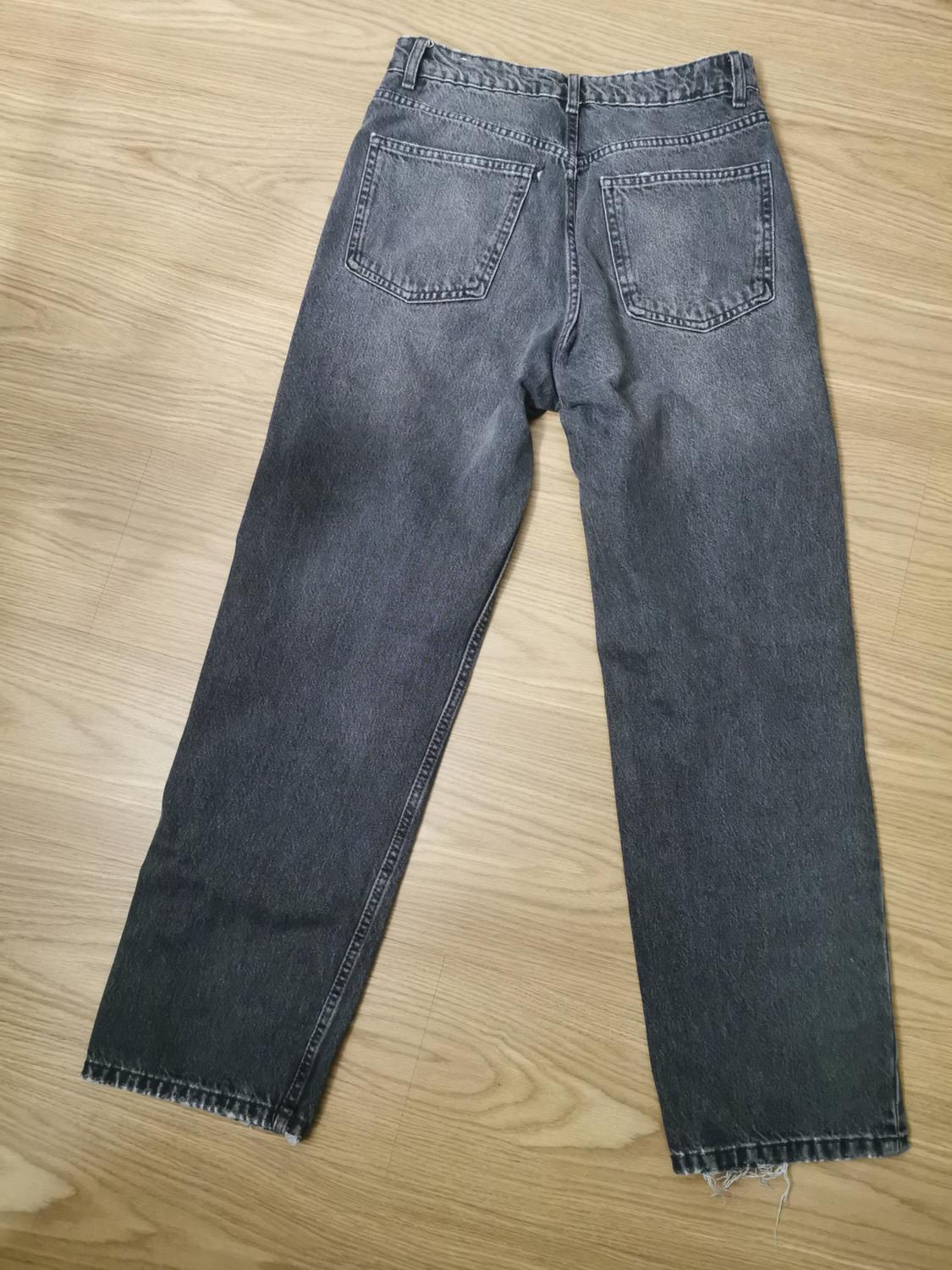 Dark grey distressed jeans, viewed from behind, with pockets and frayed hems, on a wooden floor. Relaxed and casual style.