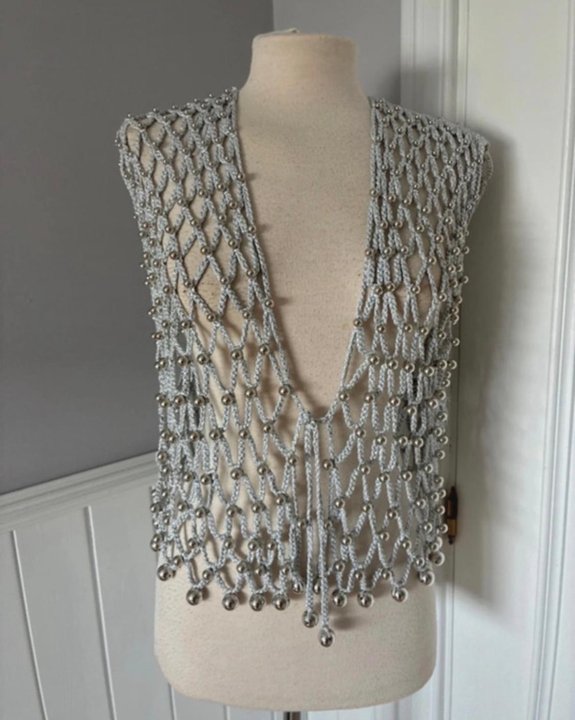 Mannequin with a grey mesh waistcoat decorated with silver beads, on a grey and white background.