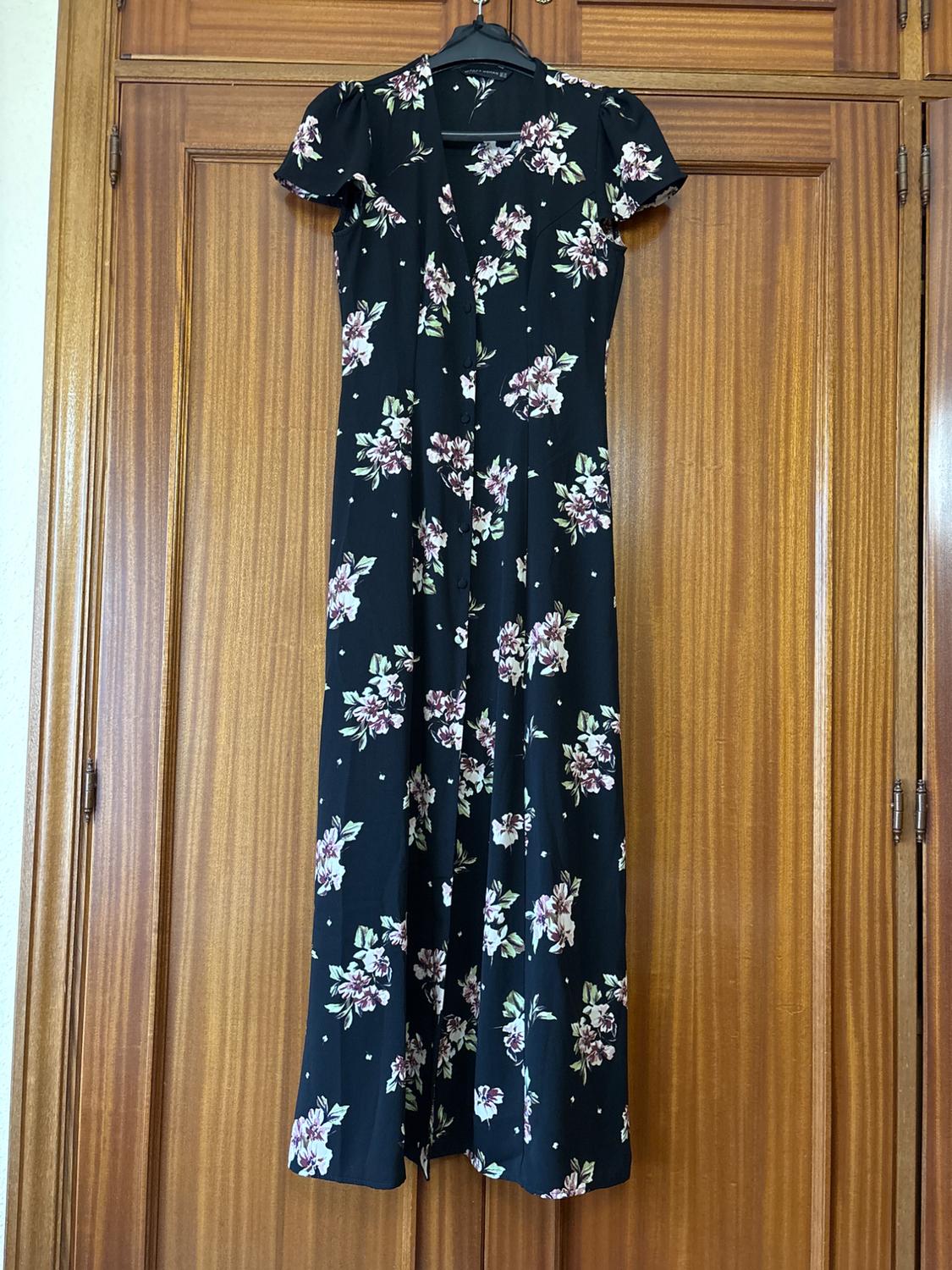 Black long dress with a floral print in pink and green hues, hanging on a wooden door.