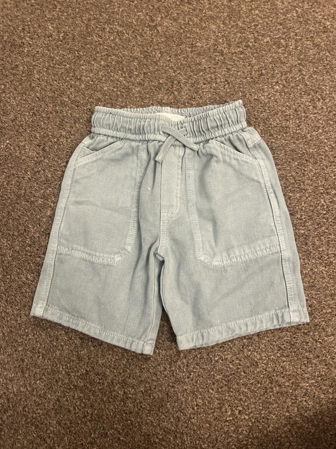 Light blue shorts with an elasticated waist, adjustable drawstring and two front pockets, on a brown carpet.