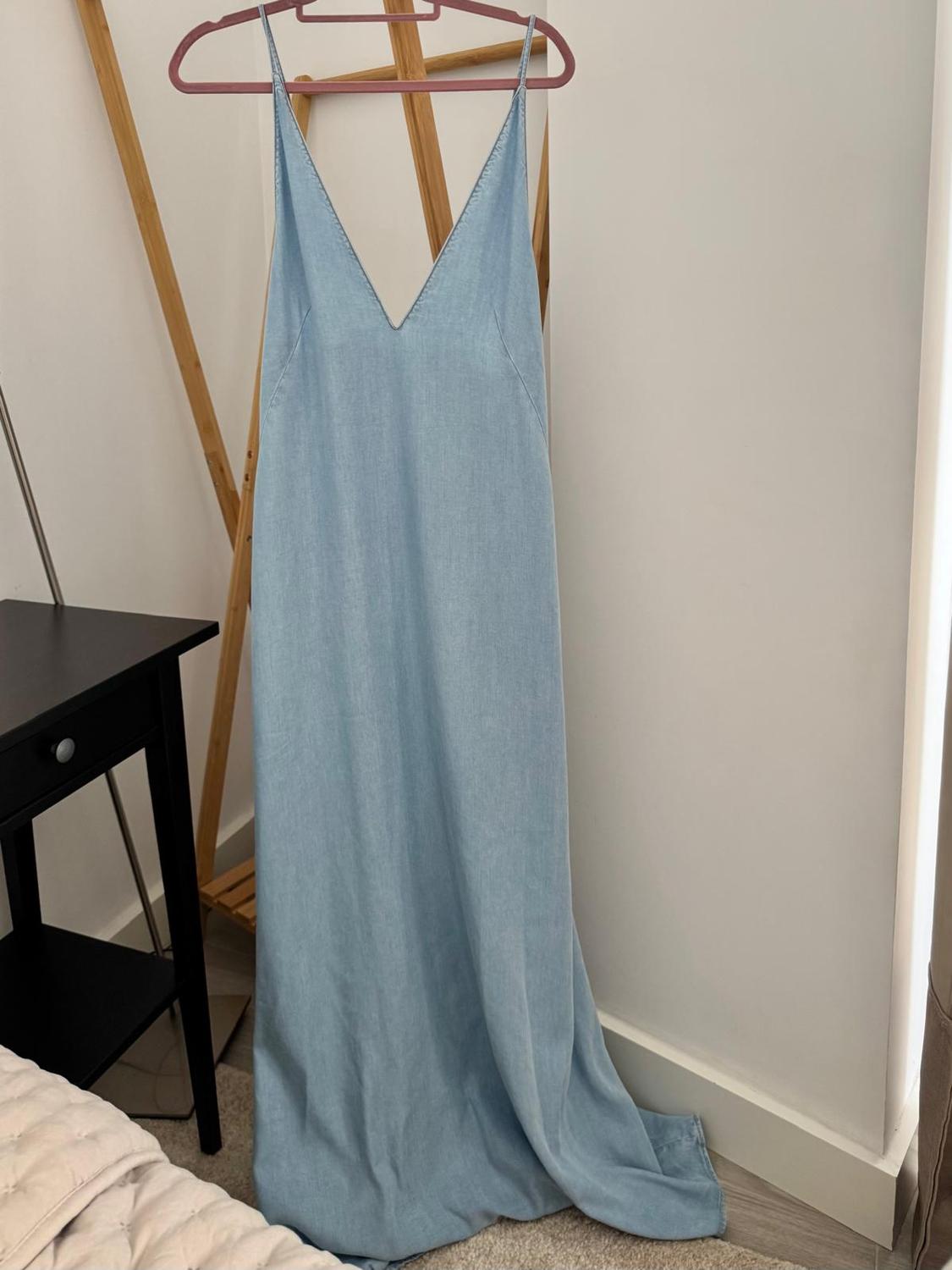 Light blue long dress with spaghetti straps and a V-neck, hanging on a pink hanger in a minimalist room.