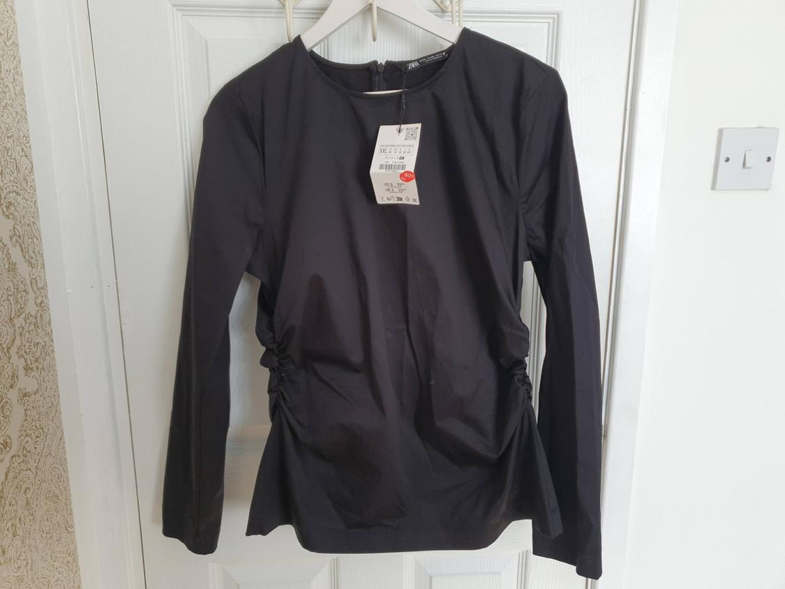 Black long-sleeved blouse hanging on a white hanger, with a visible price tag, over a white door.