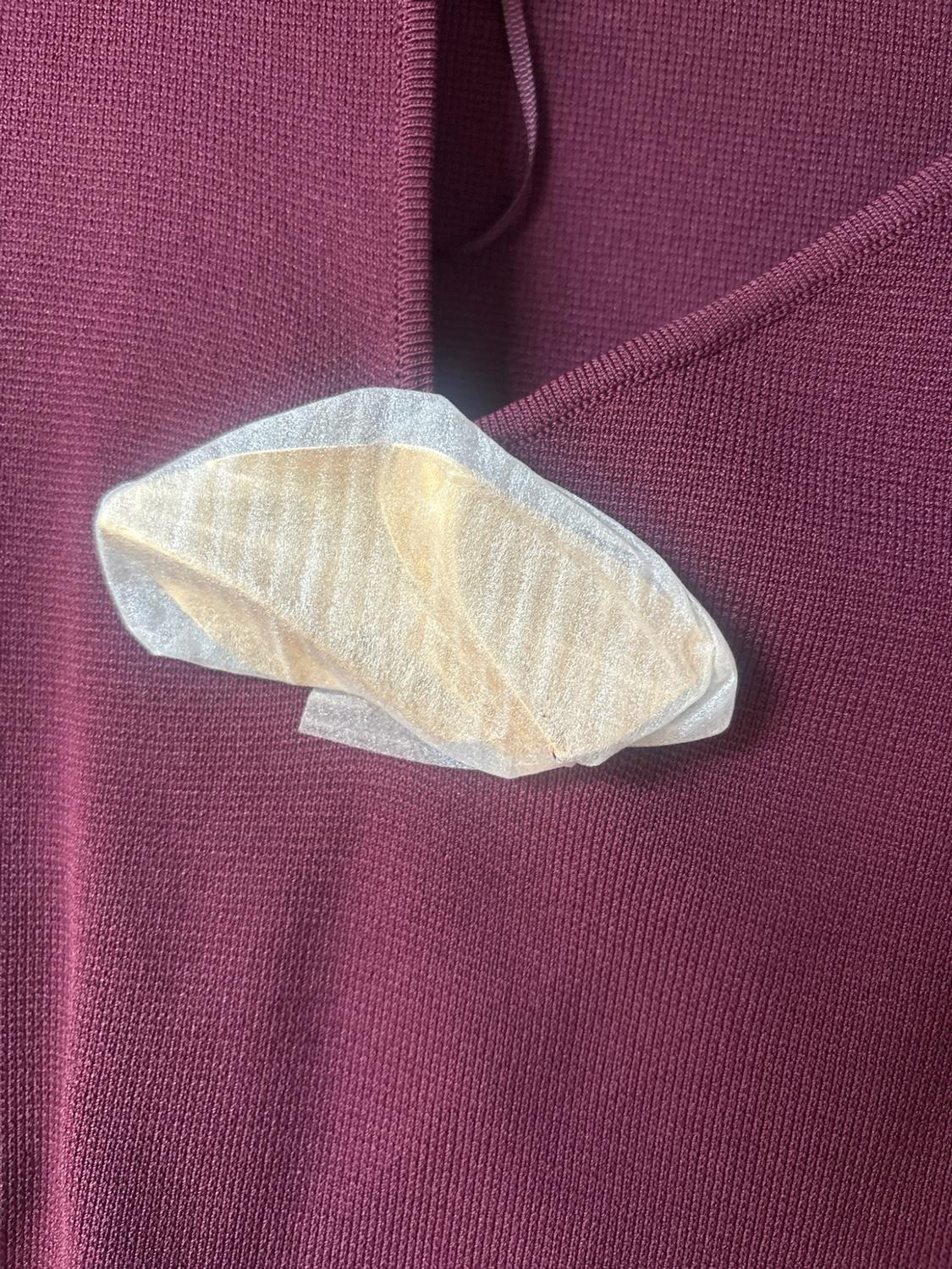 Close-up of a burgundy ribbed knit garment with a gold detail wrapped in protective paper at the neckline.