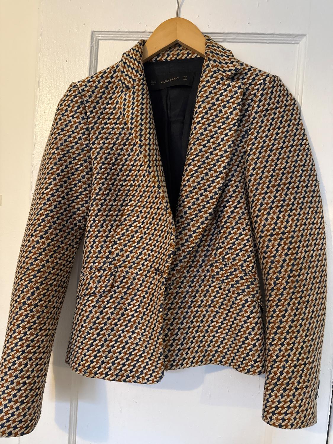 Brown and white plaid jacket hanging on a wooden hanger. Visible tag: "ZARA BASIC". White background.