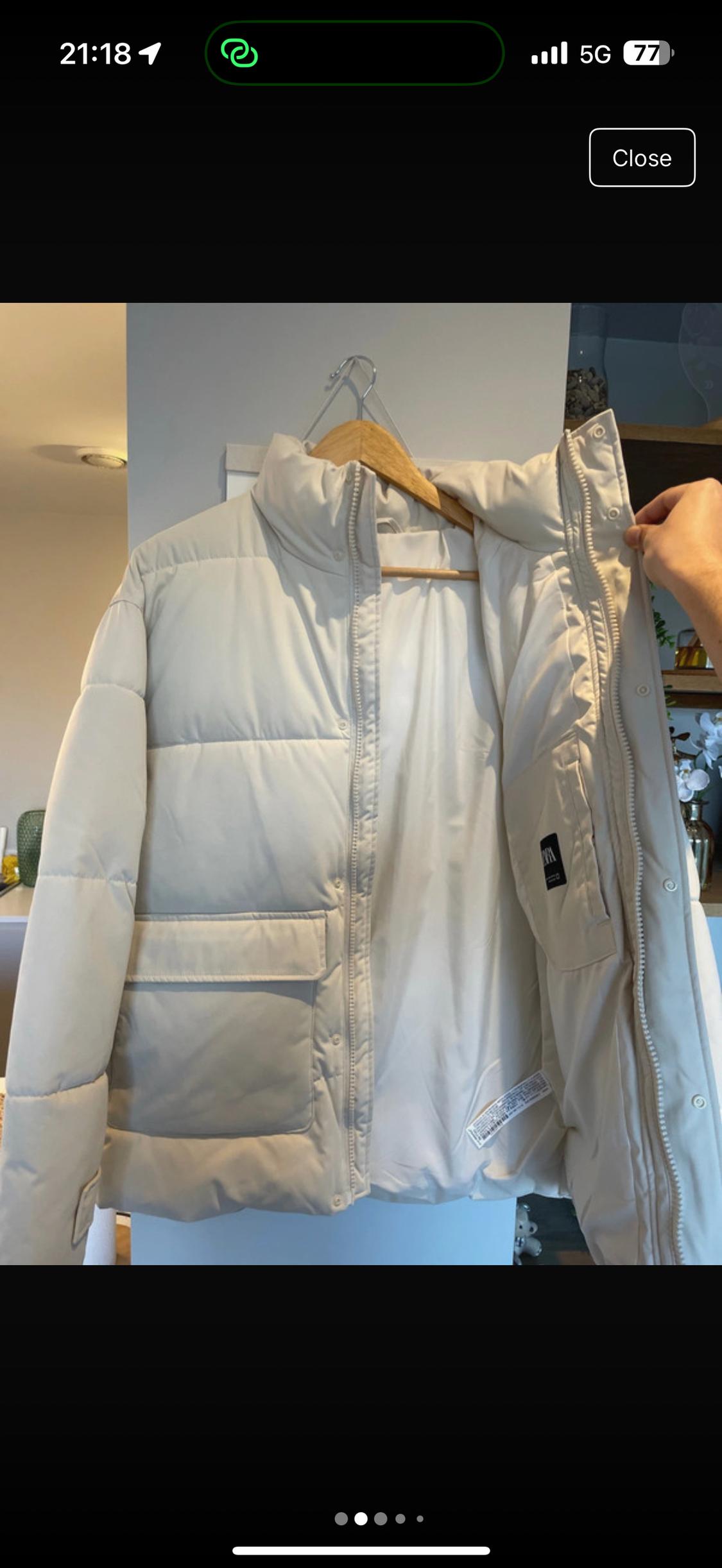 White padded jacket hanging on a wooden hanger, with an open zip and a visible pocket in an indoor setting.