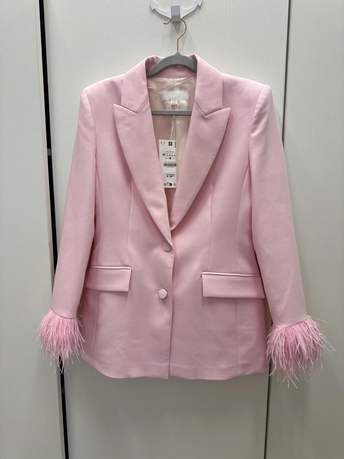 Light pink blazer on a hanger. Design with a notched lapel collar, two-button fastening, flap pockets and matching feather detail on the cuffs.