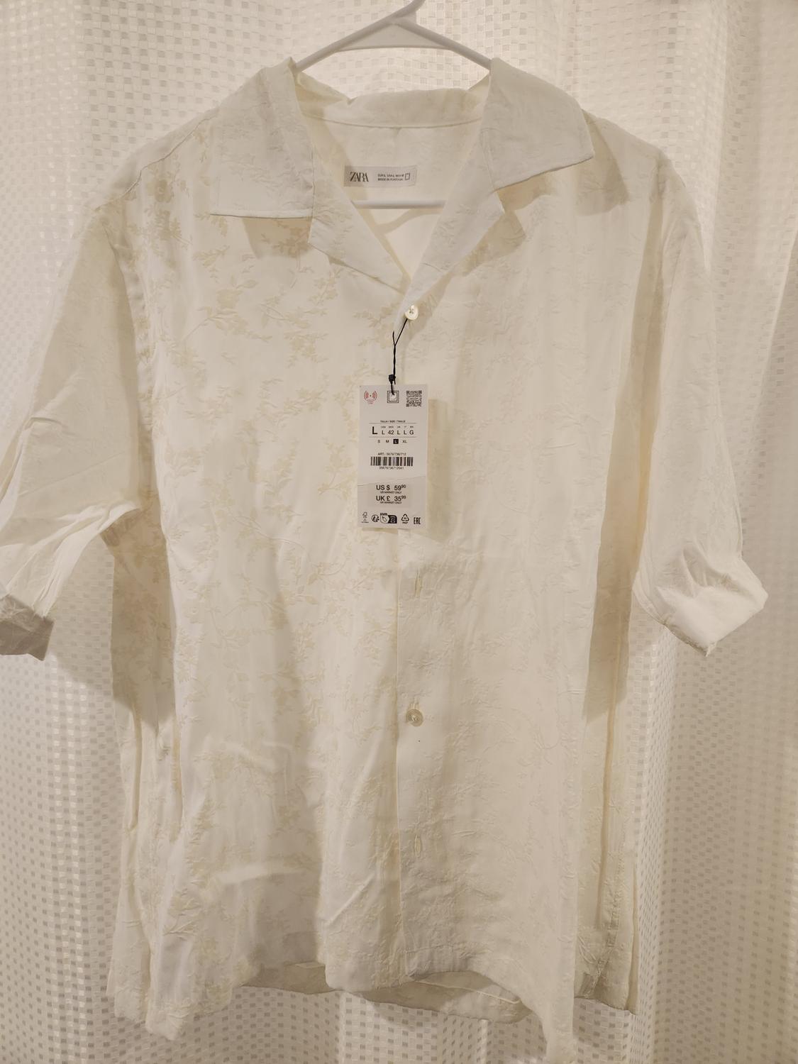 White shirt with floral texture hanging on a hanger, visible tag with price of $59.90 USD, white curtain background.