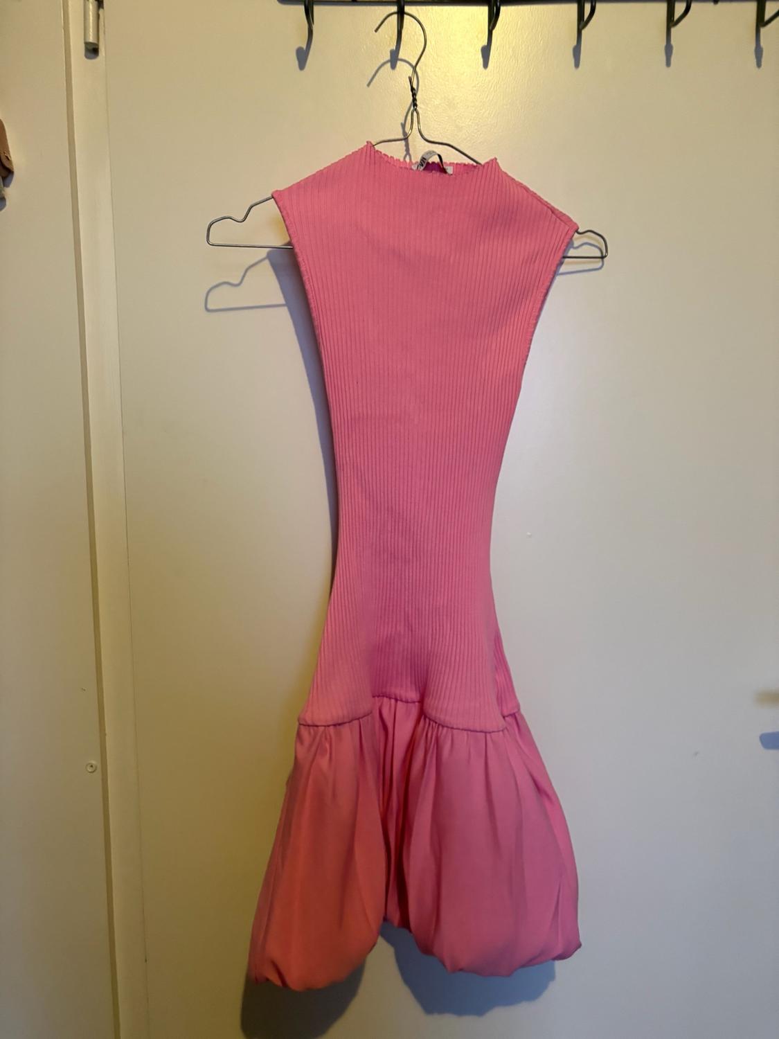 Pink ribbed knit dress with a puffball skirt hanging on a hanger over a white door.