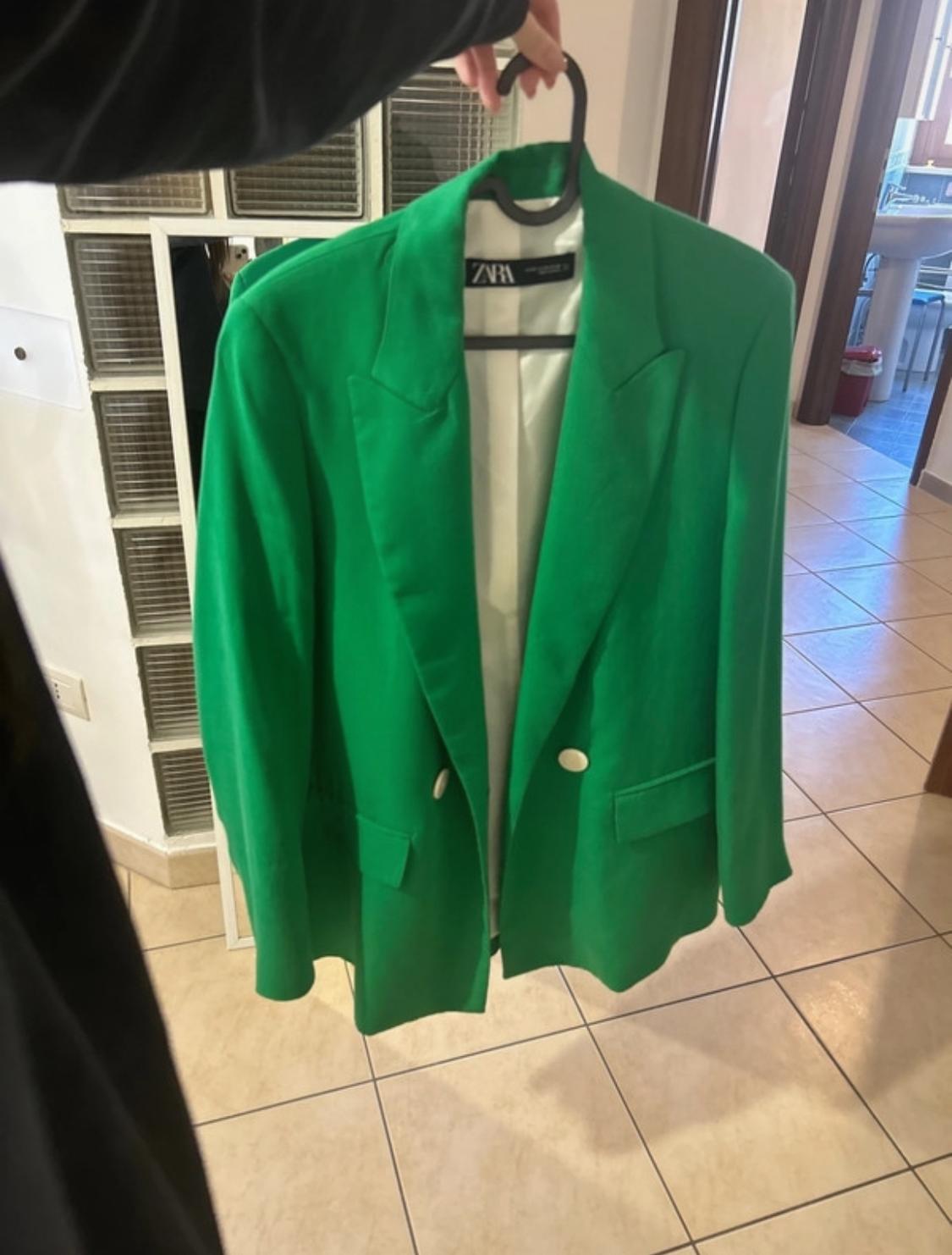 Front view of a green blazer with lapels and side flap pockets, visible white buttons.