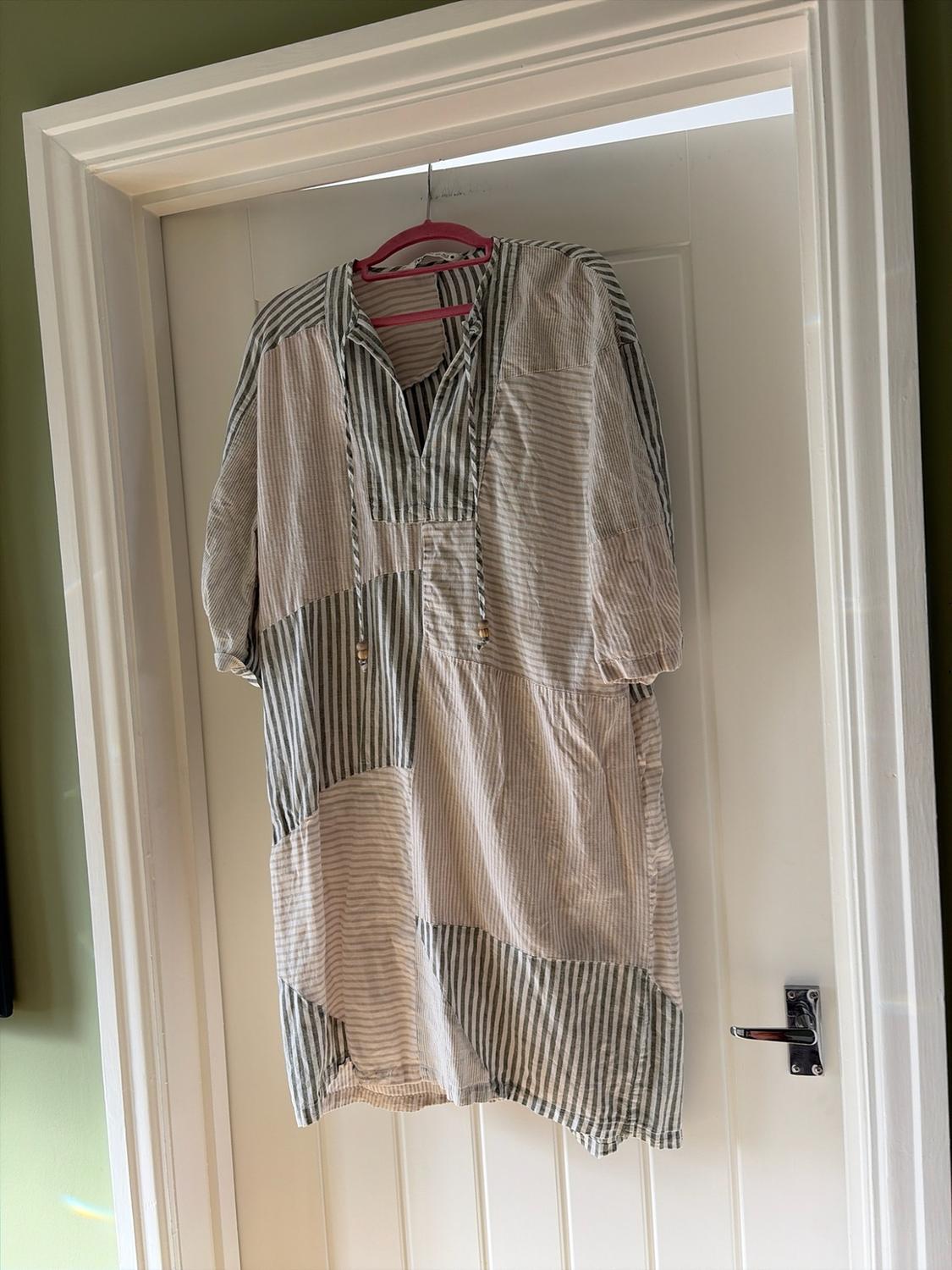 Loose-fitting short-sleeved dress with light stripe patches and a V-neck,
hanging on a hanger over a white door.