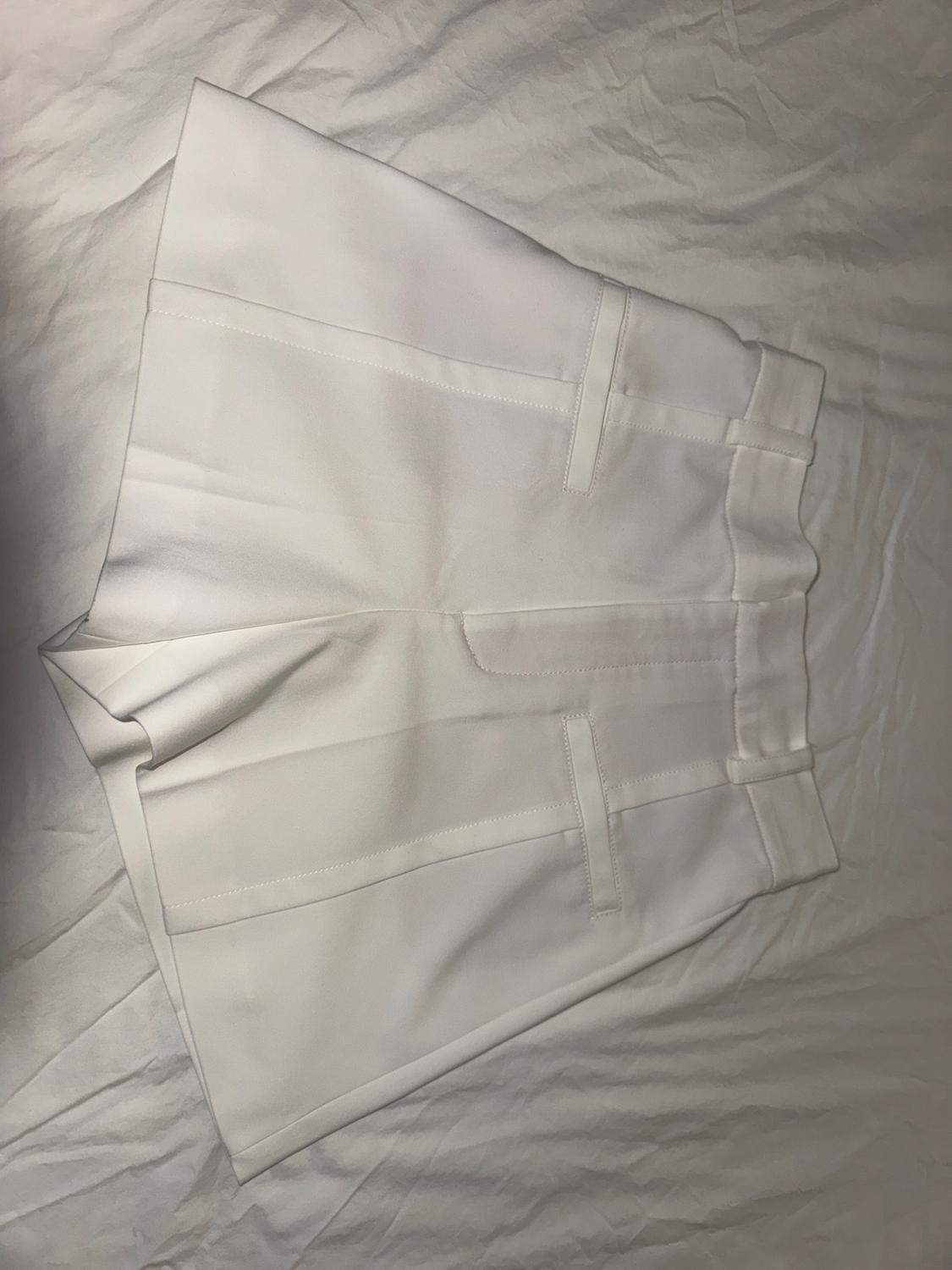 White shorts on a white wrinkled surface, with visible pockets and seams, creating a minimalist and clean style.
