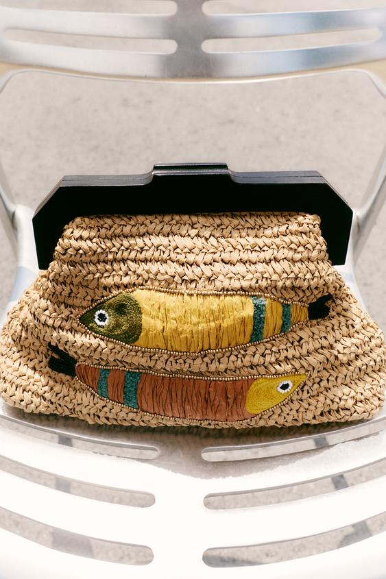 Detailní záběr opálené kabelky s výšivkou ryb ve žluté, hnědé a zelené barvě. Černá rukojeť a zacvakávací zapínání.