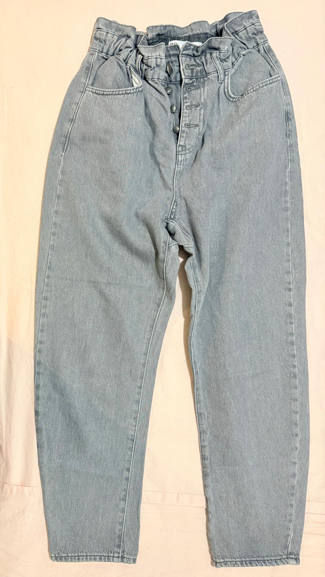 Light blue jeans with a gathered elasticated waist and front button fastening, on a light fabric background.