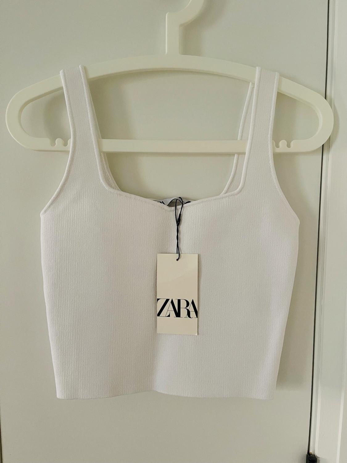 White ribbed strappy crop top with a square neckline on a white hanger. Minimalist style. Label with text ZARA.