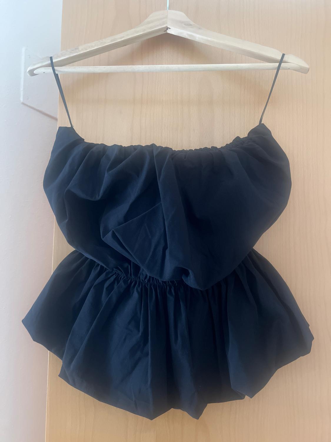 Front view of a black blouse with thin straps and frills, hanging on a hanger.