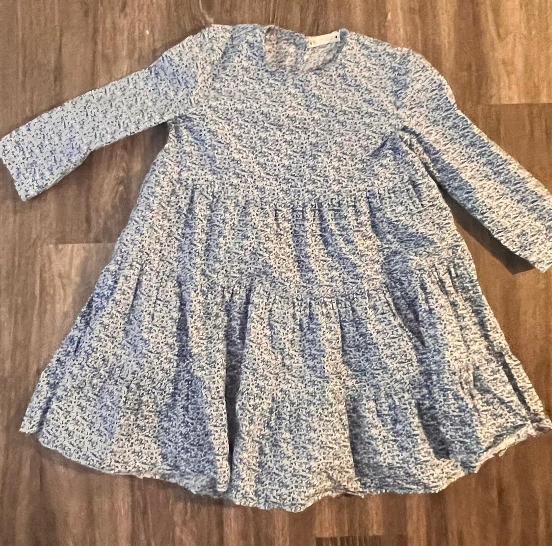 Short-sleeved, tiered, blue and white printed dress, laid out on a wooden floor.