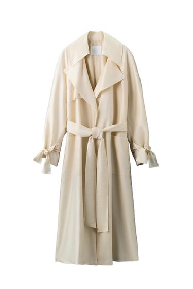 Front view of a long, ecru coat with a wide lapel, matching belt, and long sleeves with ties at the cuffs.