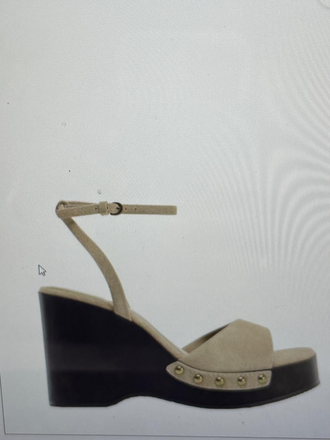Beige sandal with black wedge sole, profile view. Features a wide strap, ankle strap with buckle, and studs on the platform.