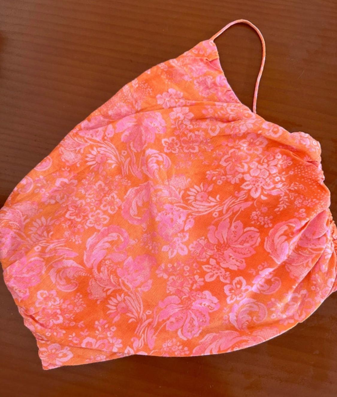 Orange top with a pink floral print, thin straps and side ruching, on a wooden surface.