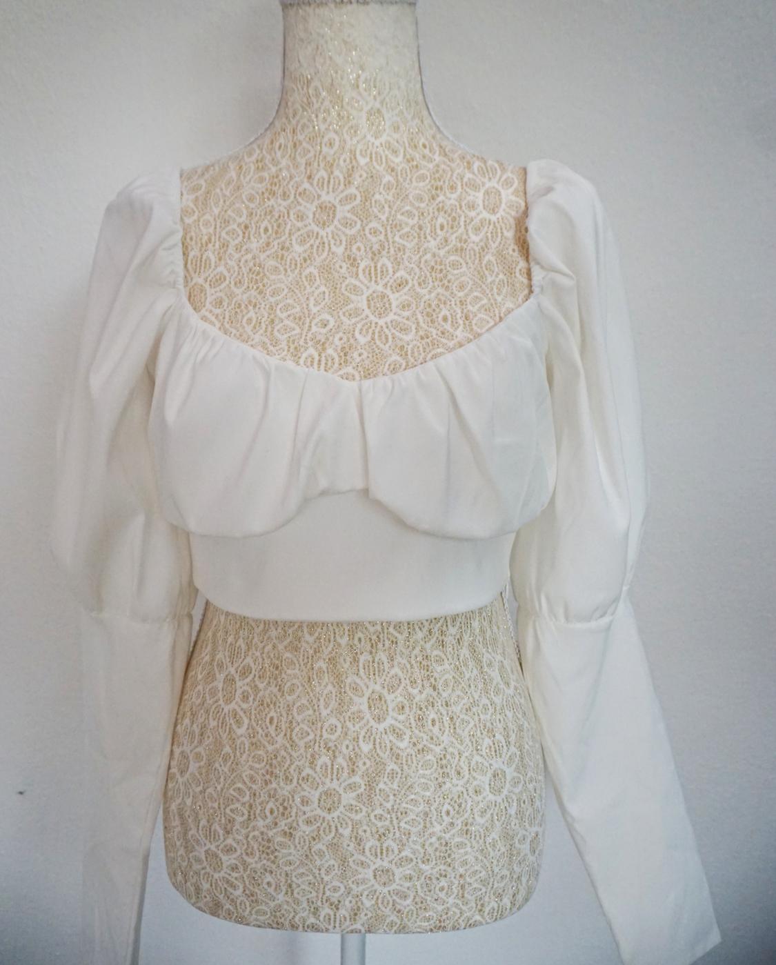 White crop top with long puff sleeves and a gathered neckline, displayed on a mannequin with a floral lace design on a light background.