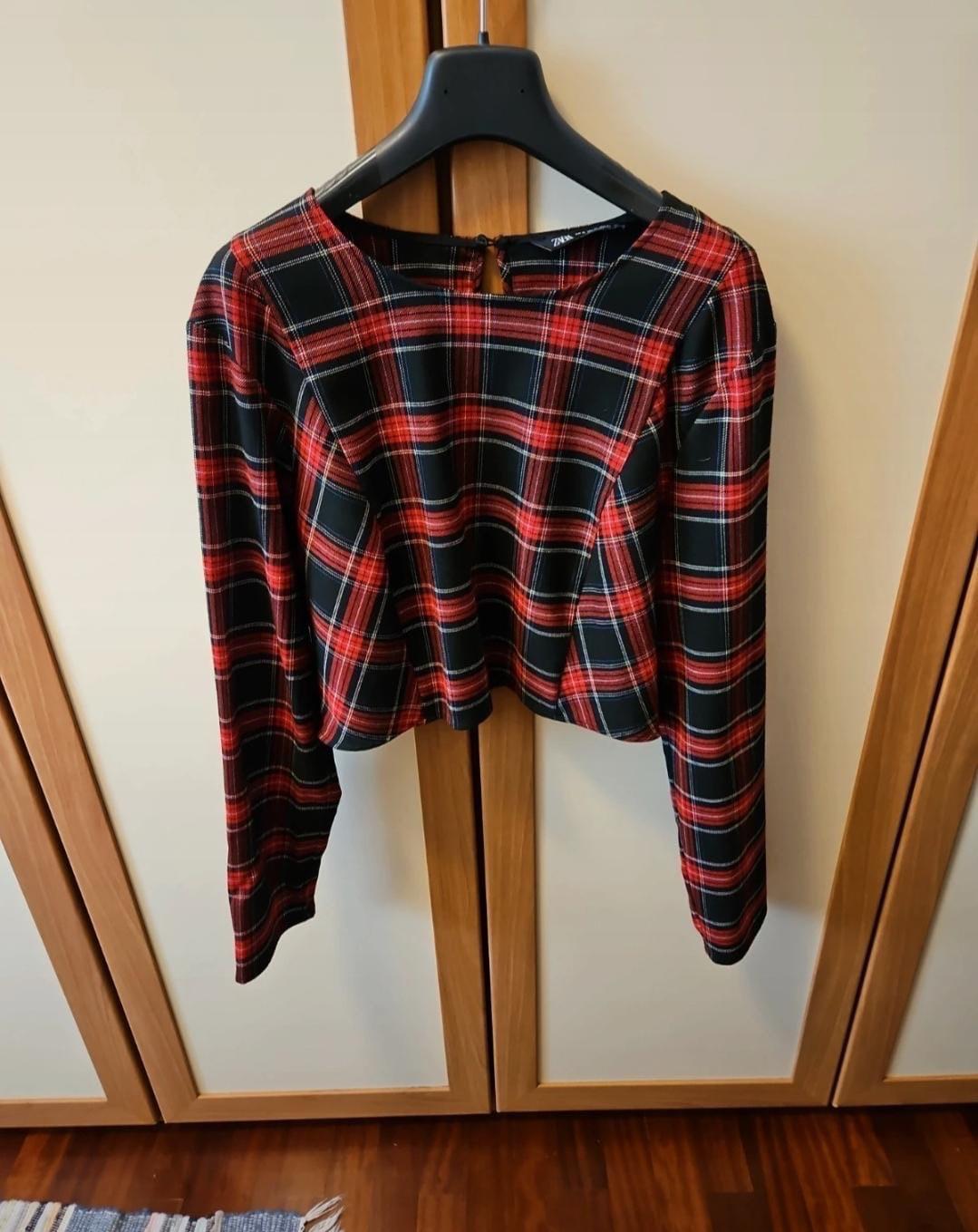 Red and black checked blouse hanging on a black coat hanger in front of a light wood wardrobe.