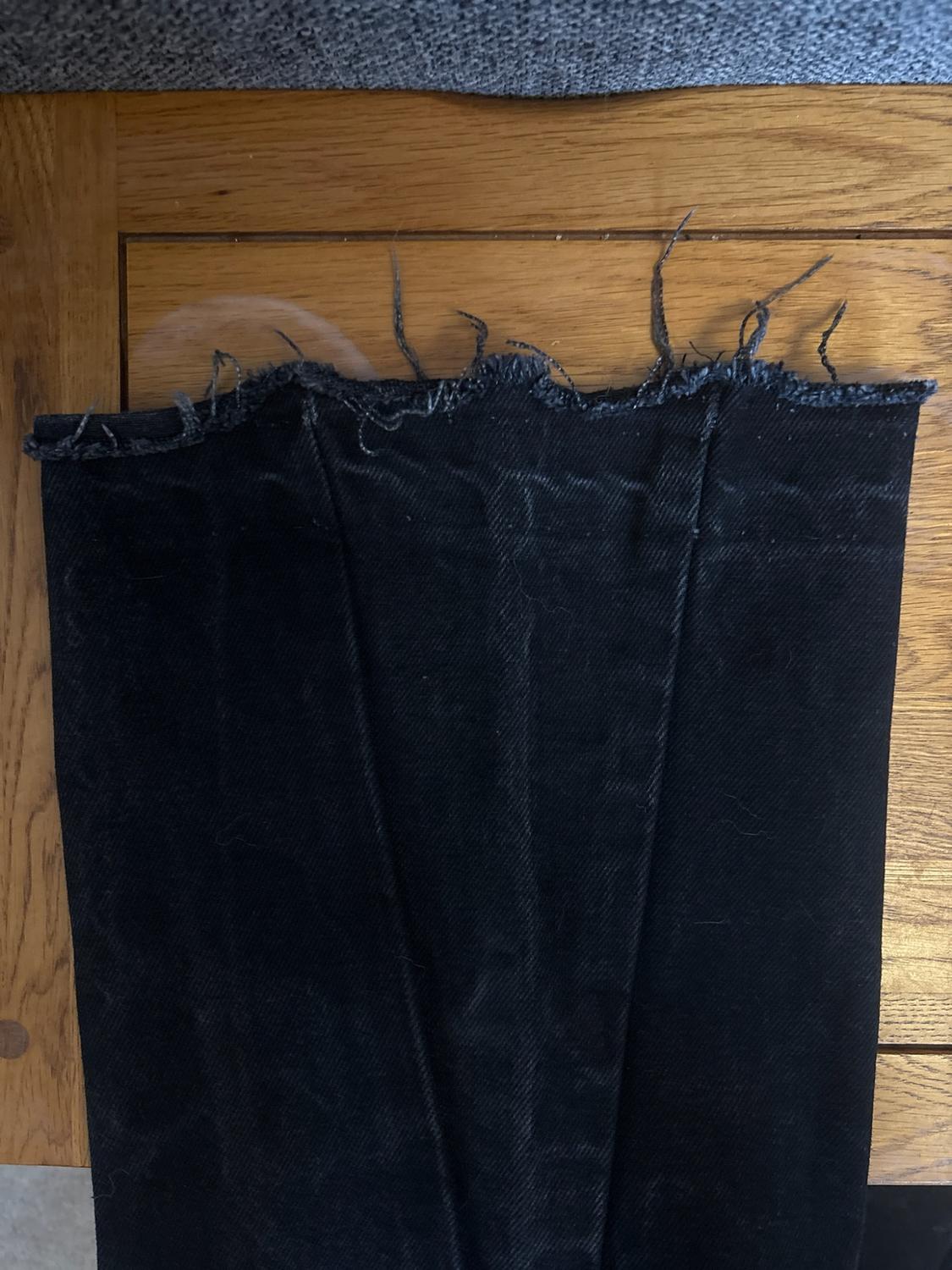 Close-up of the frayed hem of a pair of black jeans on a wooden surface.