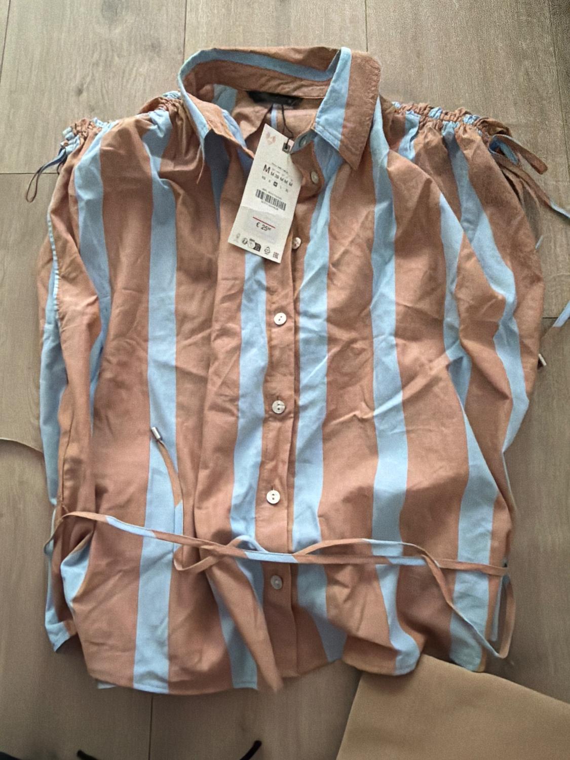 Blue and brown pinstriped shirt with price tag on light wooden floor.
