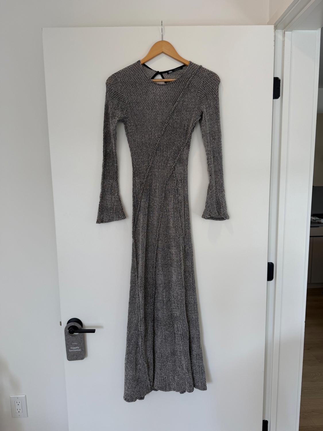 Textured grey maxi dress with long sleeves, hanging on a hanger over a white door. Minimalist setting.