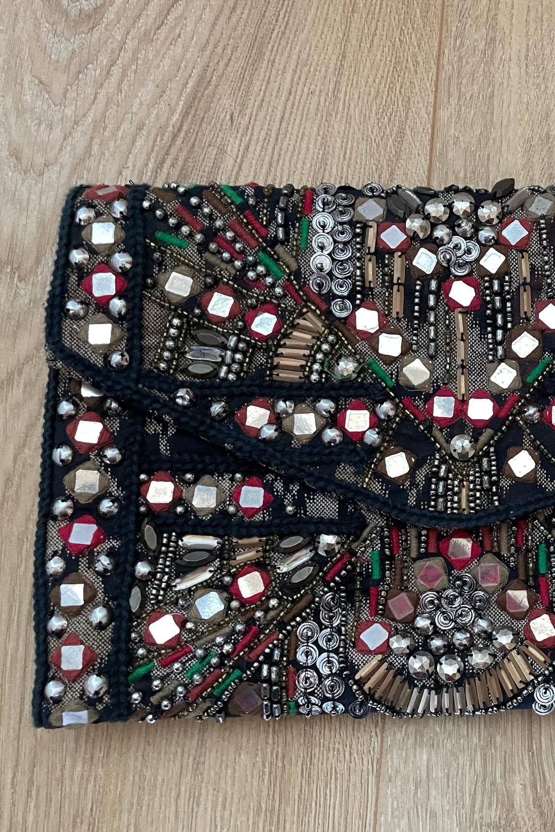 Handbag detail with beads and metallic embellishments in shades of red, green, and black.