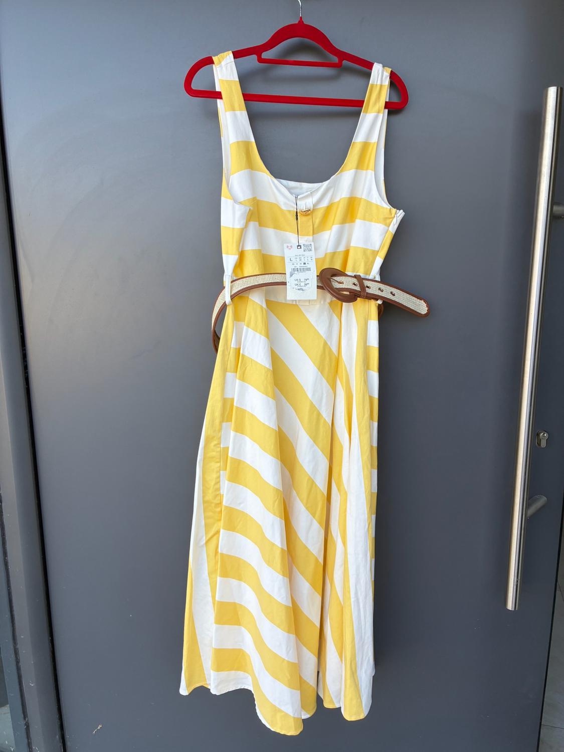Yellow and white striped dress with a brown braided belt, hanging on a red hanger on a grey door.