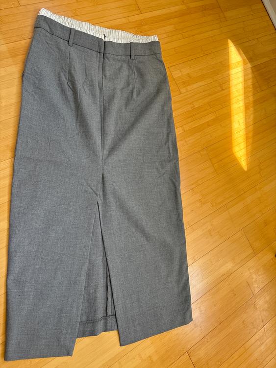 Light gray fabric skirt with a front slit, visible white elastic waistband, on a light wood floor illuminated by natural light.