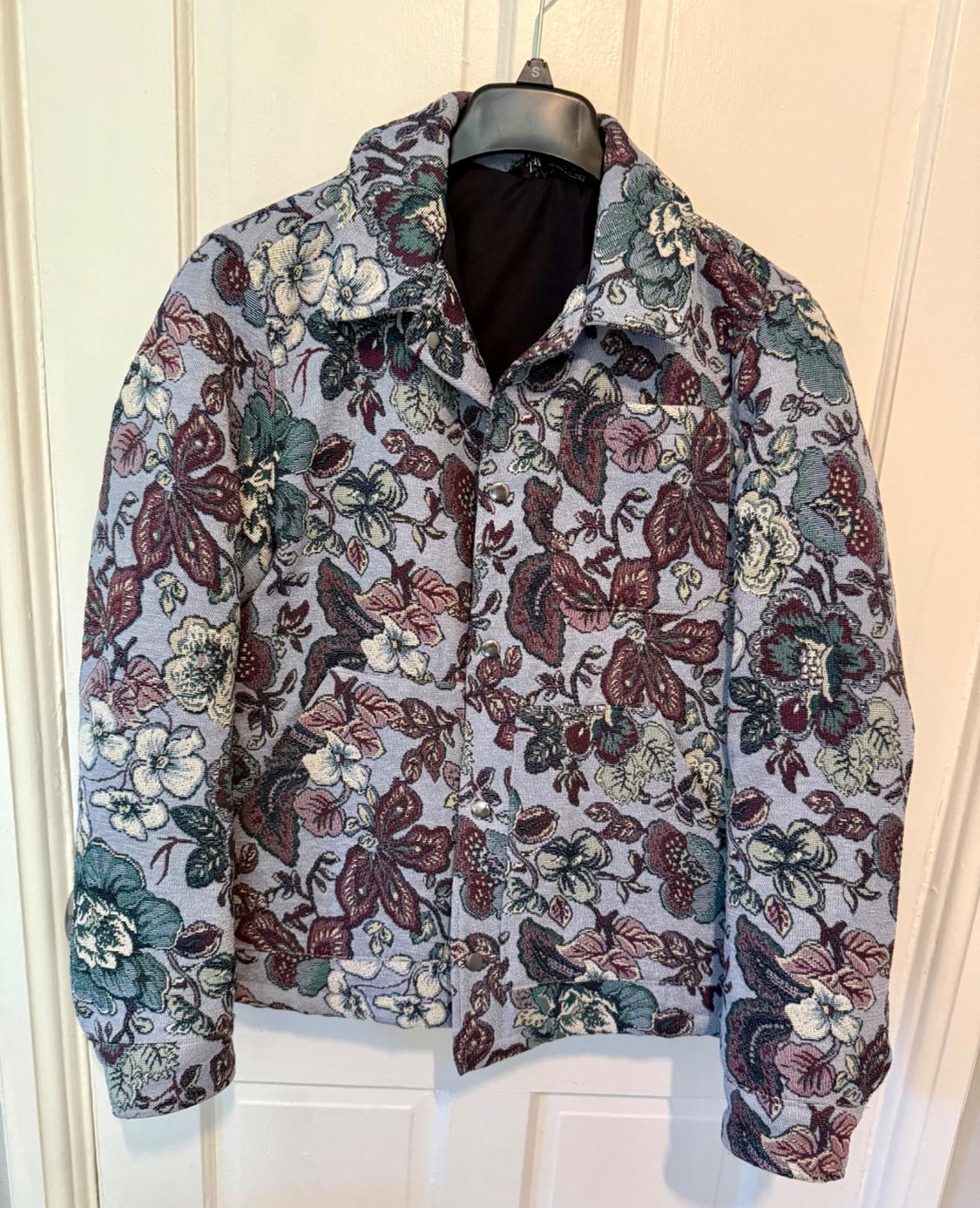 Hung jacket with floral print in shades of burgundy, green and white on a grey background. White door background.