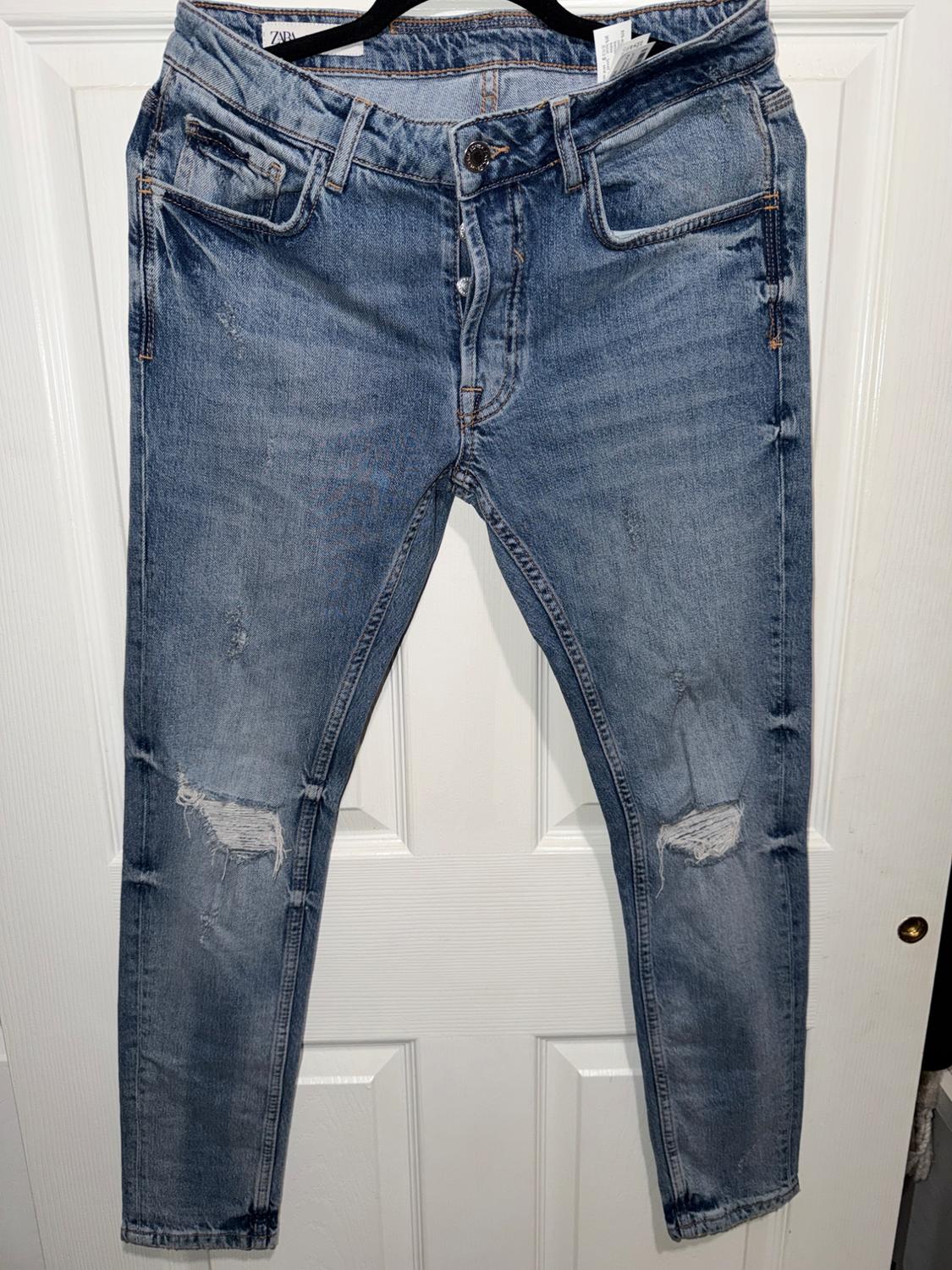 Worn blue jeans hanging on a hanger in front of a white door. Visible front pockets and ripped detailing.