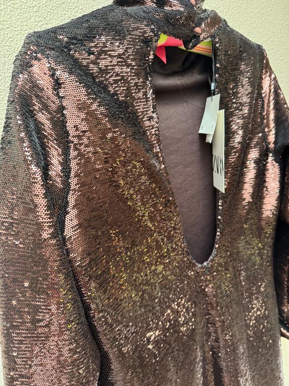Brown sequin dress with V-neck, hanging on a hanger. Visible tags with the text "ZARA".