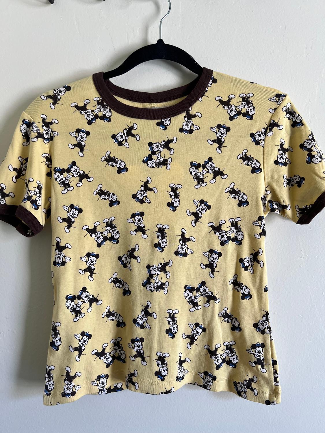 Yellow T-shirt with a repeated black and white cartoon character print, hanging on a black hanger.