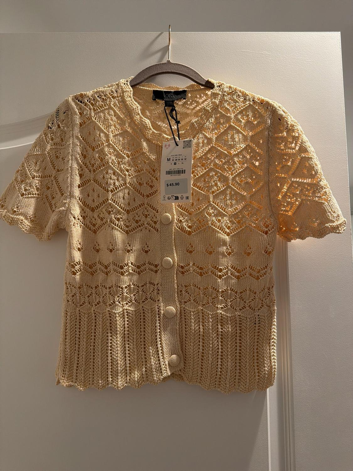 Cream knit cardigan with short sleeves and front buttons. Features a lace-knit pattern. Price tag with "M" and "$45.90" visible.