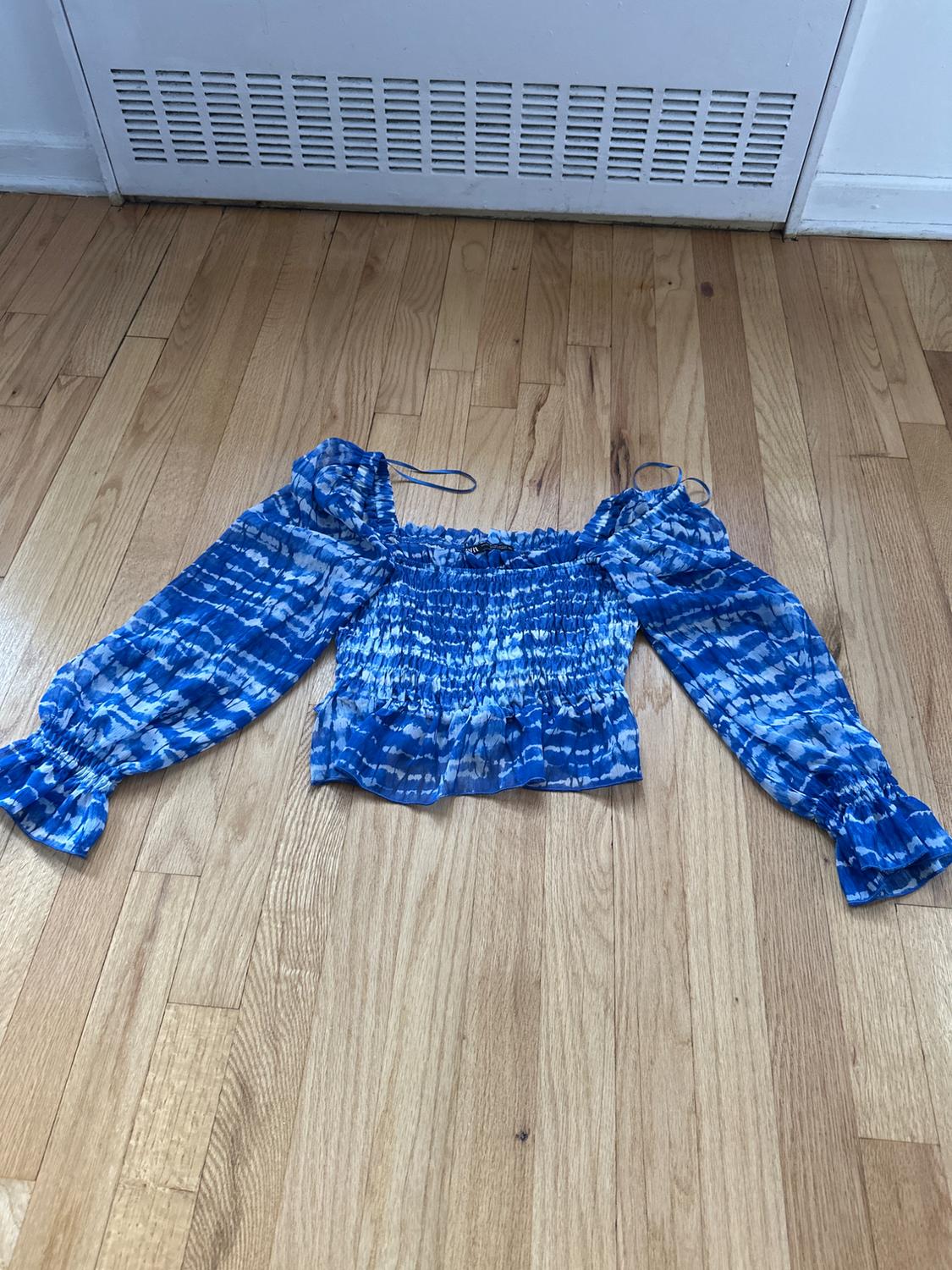 Front view of a blue blouse with a tie-dye print and long puff sleeves.