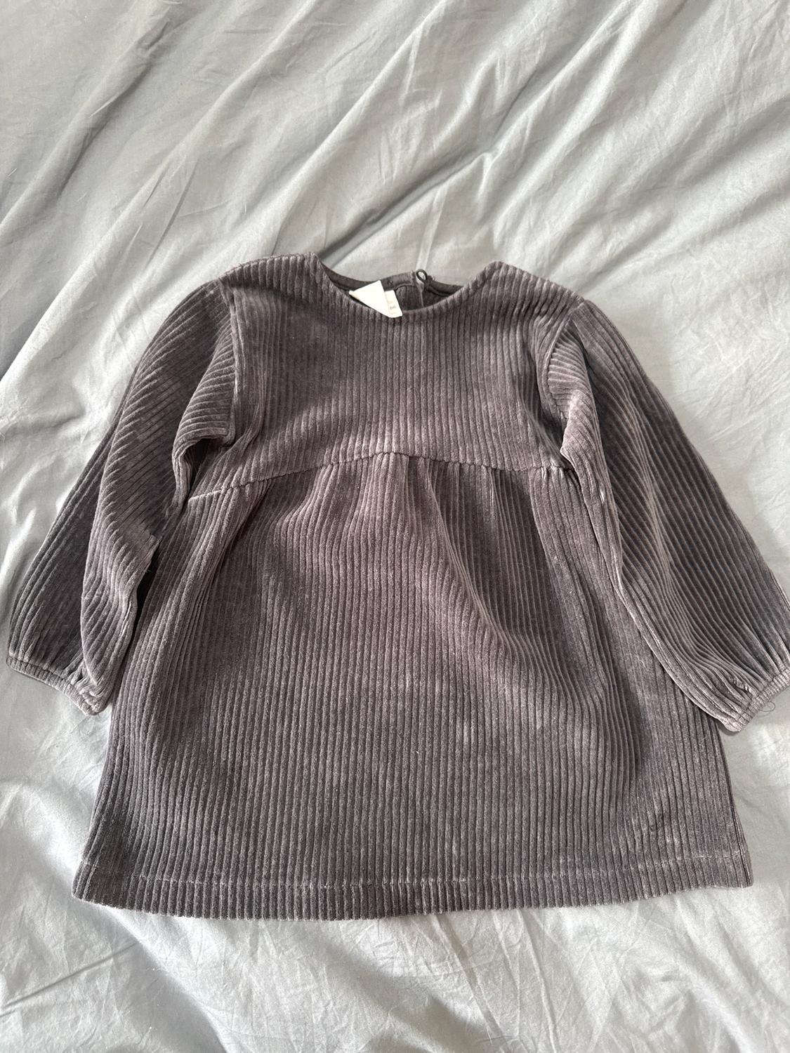 Grey corduroy dress with long sleeves and a round neck, on a crumpled grey sheet.