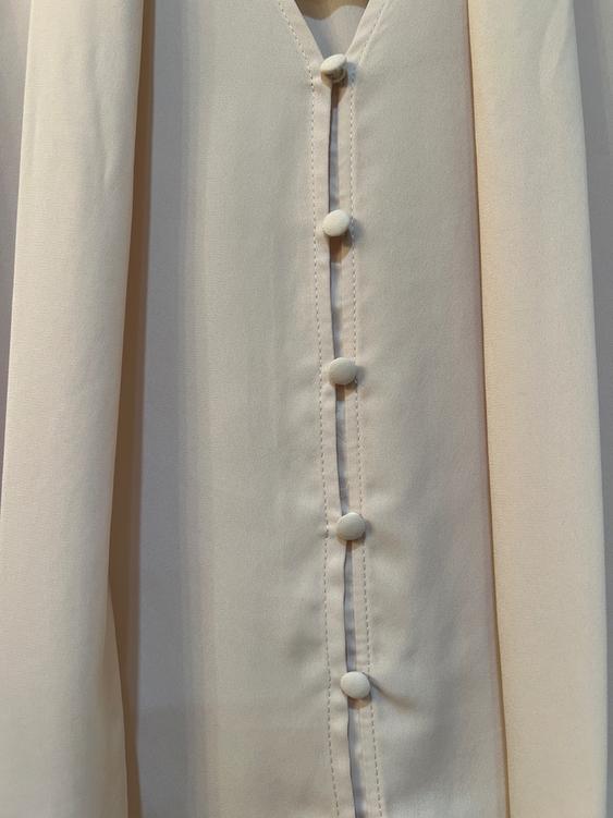 Detail of a beige blouse with fabric-covered buttons, showing seams and soft texture.