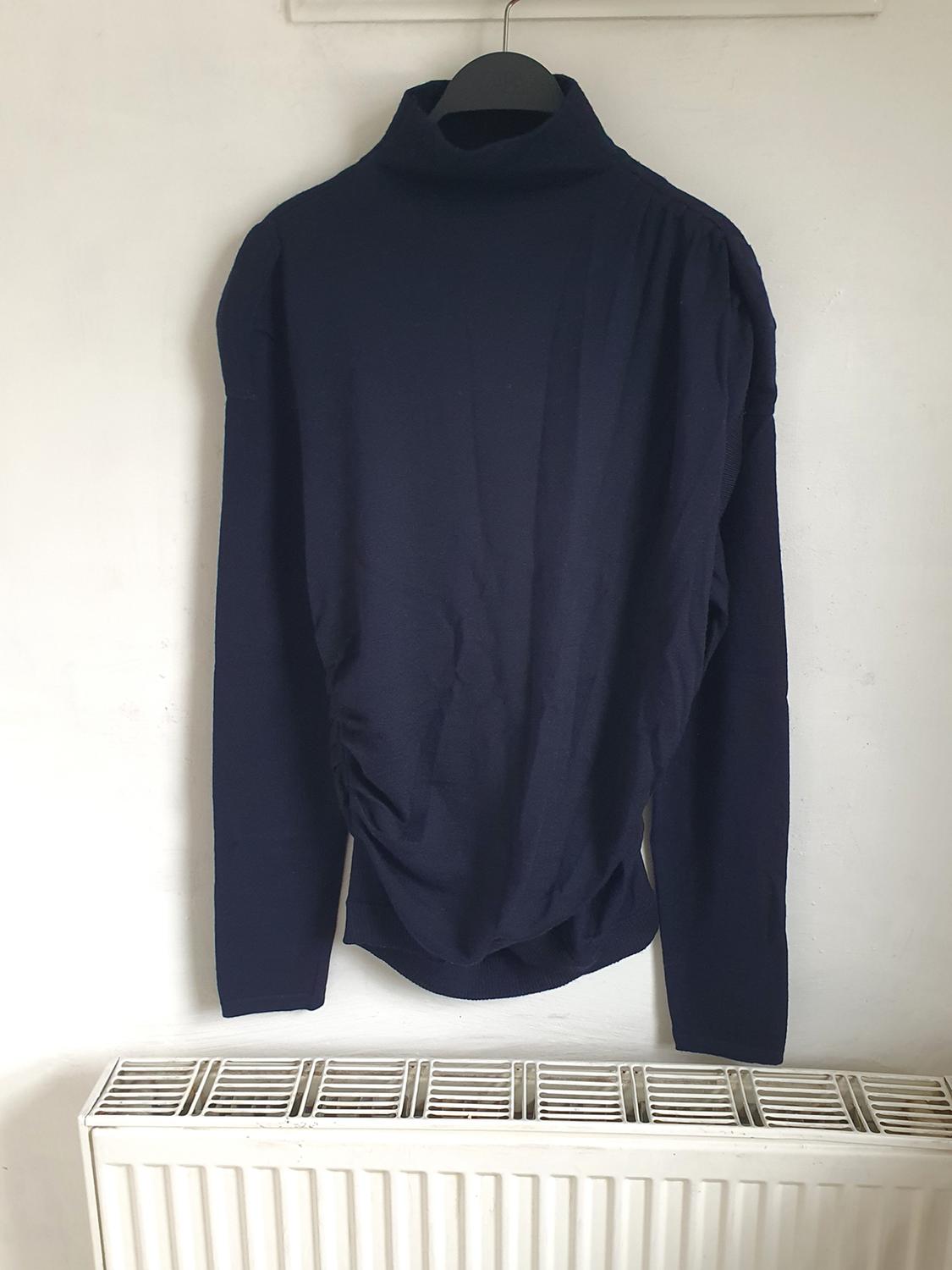 Dark blue roll-neck jumper hanging on a black hanger on a white wall, above a white radiator.