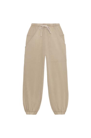 Front view of beige jogger trousers with an adjustable elasticated waistband, patch pockets, and elasticated cuffs at the hems.